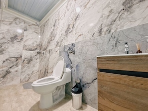 Ein Badezimmer mit einer Marmorwand, einer weißen Toilette, einem Holzwaschtisch und einem Mülleimer.