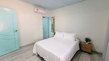 A bedroom with a bed, a nightstand, a potted plant, a door, and an air conditioning unit.