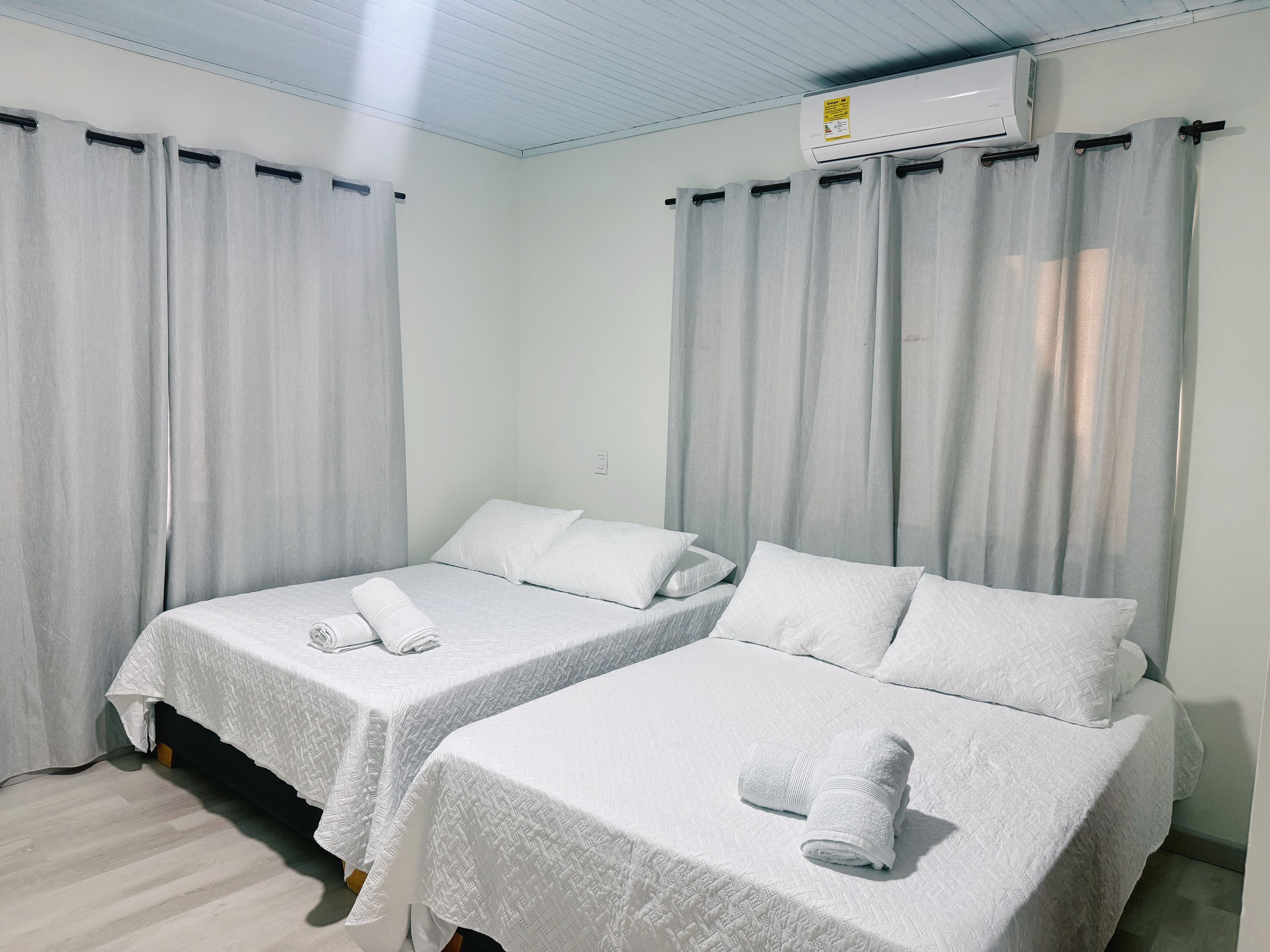 Ein Hotelzimmer mit zwei Betten, jedes mit einem zusammengerollten Handtuch, weißer Bettwäsche und einer Decken-Klimaanlage.
