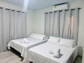 Ein Hotelzimmer mit zwei Betten, jedes mit einem zusammengerollten Handtuch, weißer Bettwäsche und einer Decken-Klimaanlage.