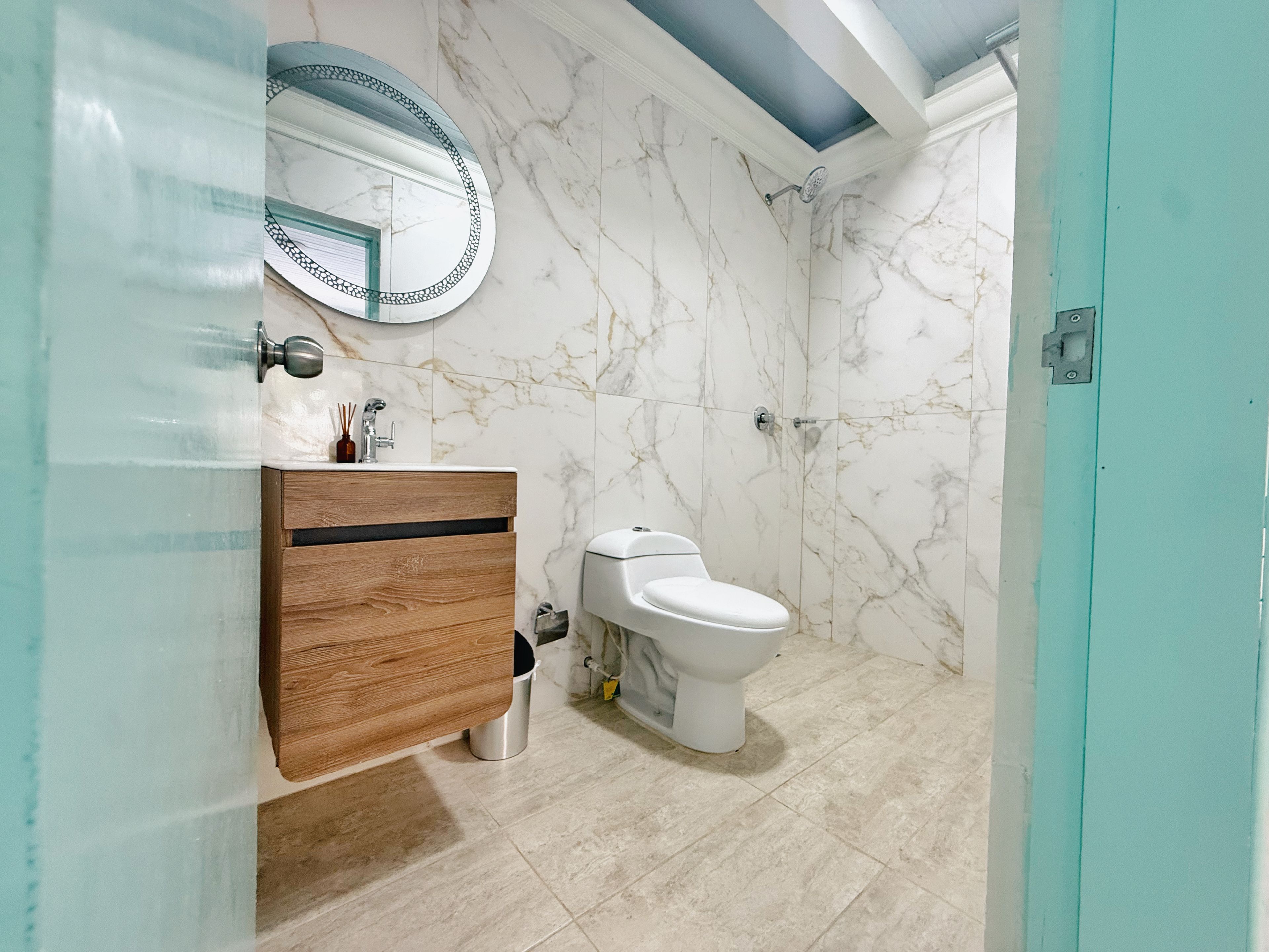 Un baño con pared de mármol, tocador de madera, inodoro y zona de ducha.