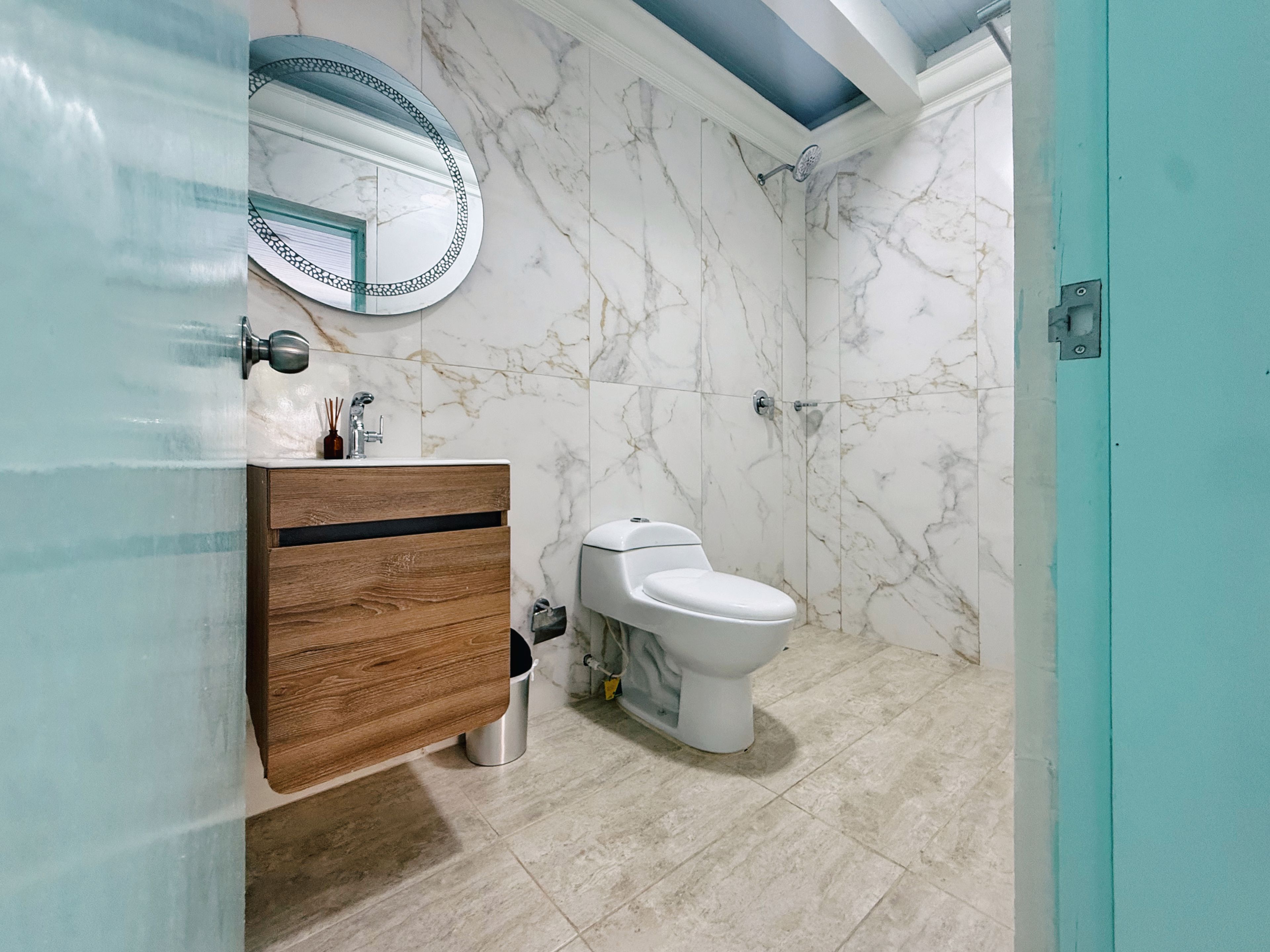 Ein Badezimmer mit Marmorwand, Waschtisch aus Holz, Toilette und Dusche.
