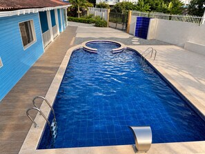 Una piscina rectangular amb un videtell daurat, envoltada per un sòl de formigó, a prop d'un edifici blau amb teulada emblenquinada.
