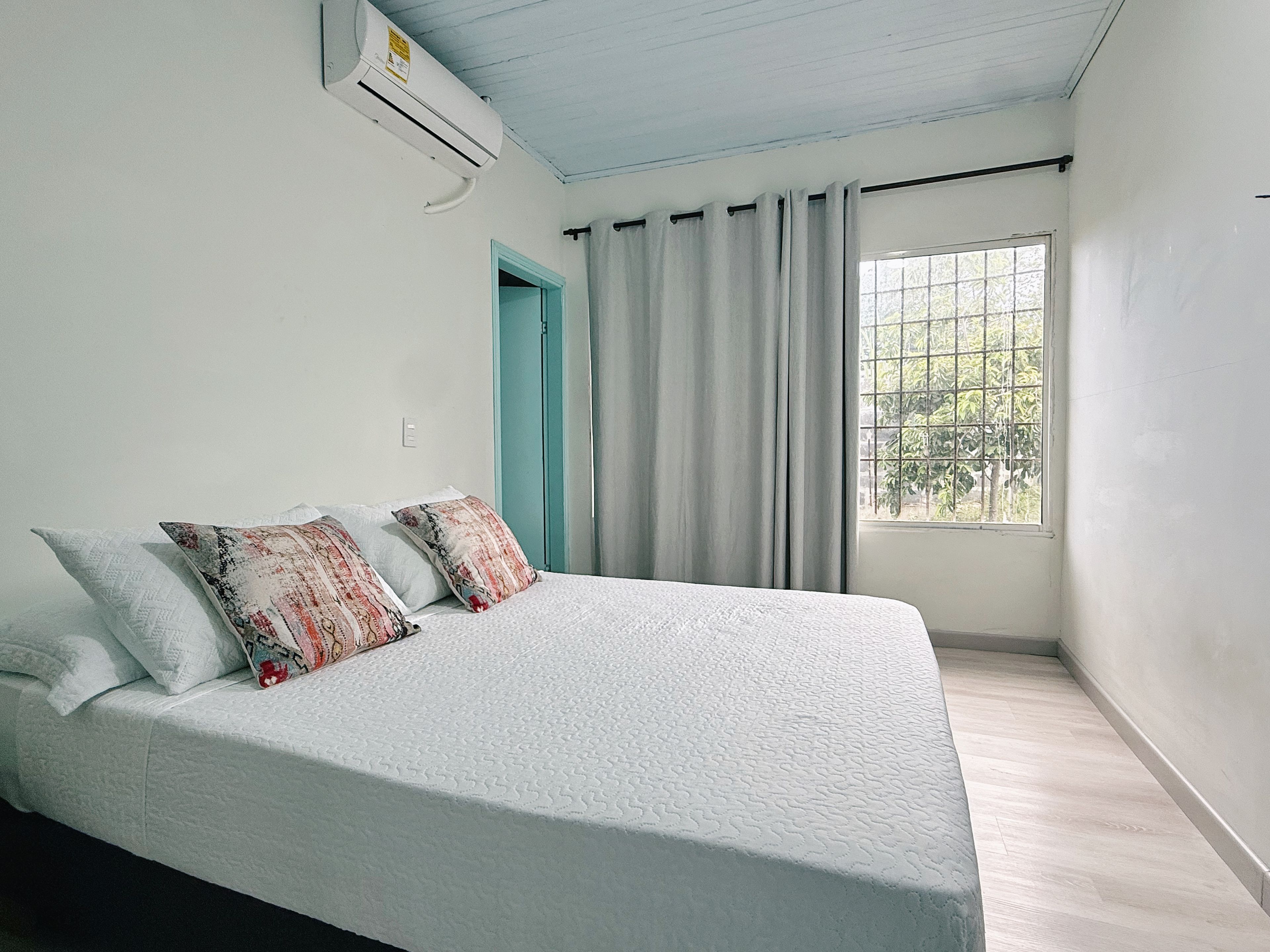 Een slaapkamer met een bed, een raam met gordijnen en een airconditioning.