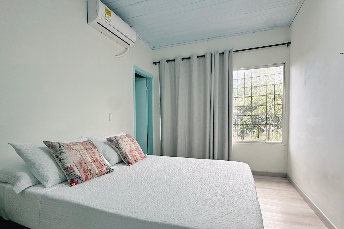 A bedroom with a bed, a window with curtains, and an air conditioning unit.