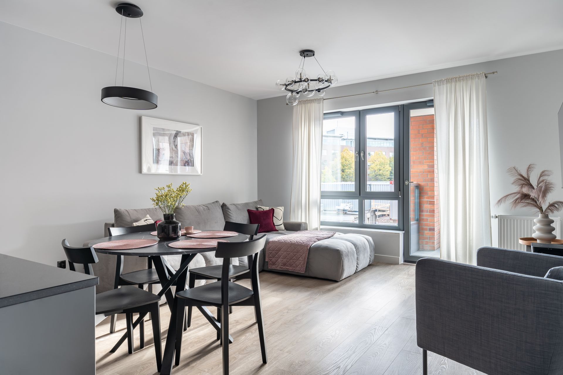 A modern living room with a dining area, a sofa set, and a large window with a view of buildings.