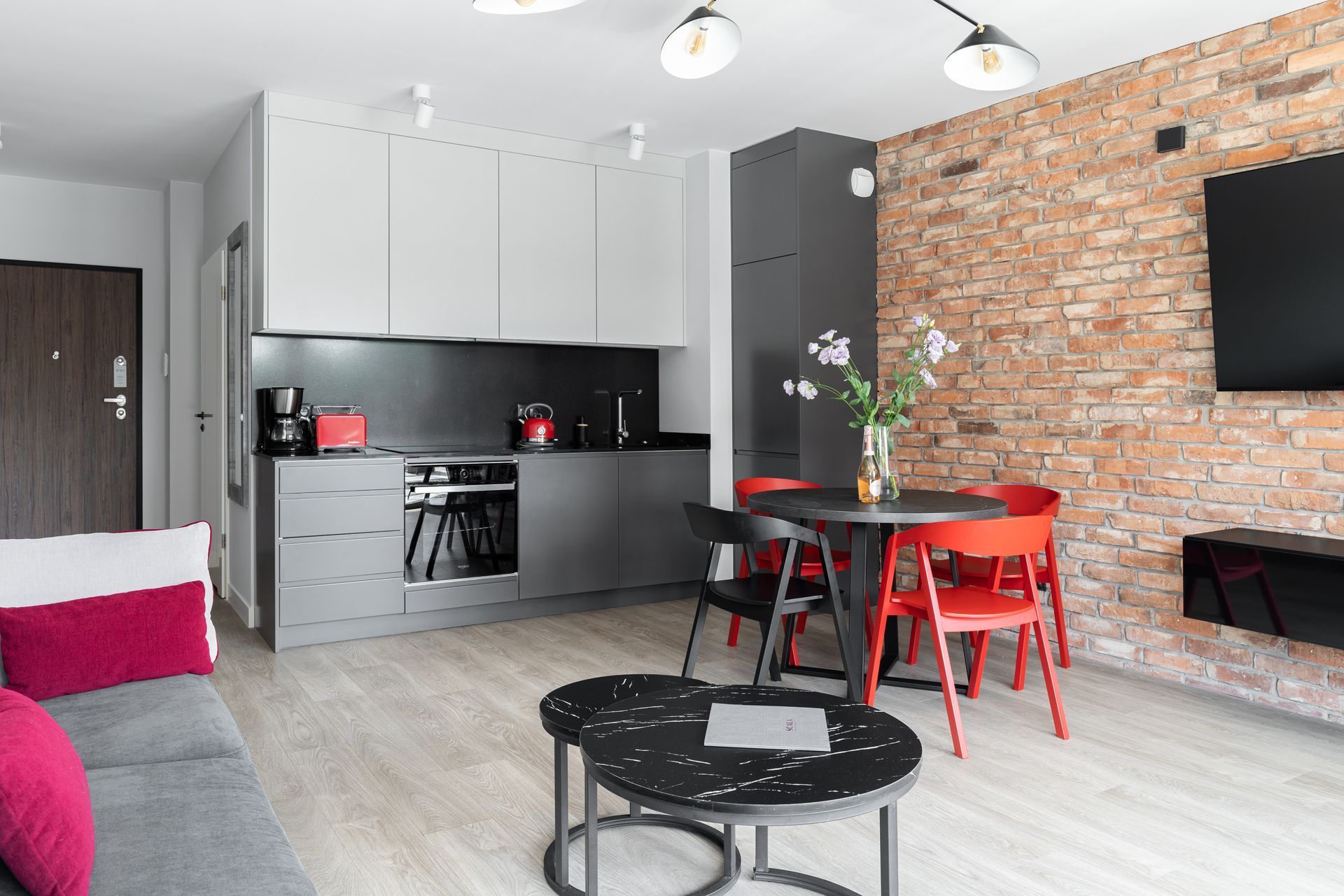 A modern kitchen with grey cabinets, a black countertop, and a red kettle.