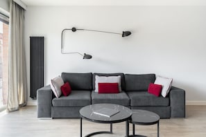 Una sala moderna con un sofá gris, dos mesitas negras y una lámpara de pie negra.
