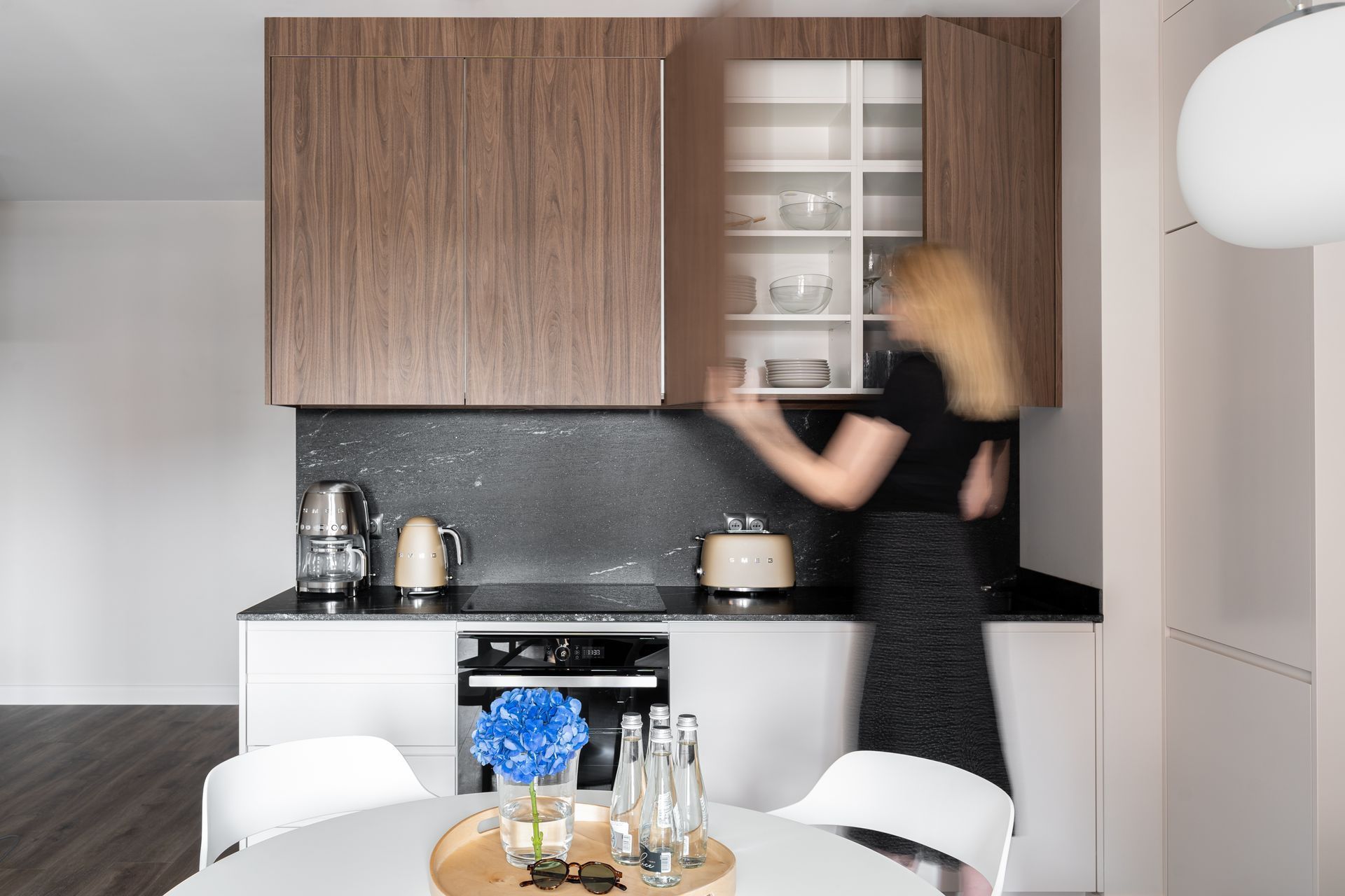 A modern kitchen with wooden cabinets, a black countertop, and a dining area with a white table.