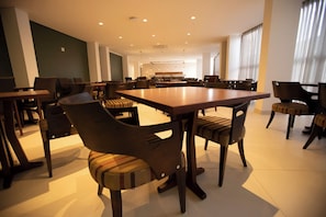 A spacious dining area with multiple tables and chairs, a kitchen in the background, and large windows allowing natural light. - Modern Space Near Araripina Botanical Garden and Araripe Regional Airport (Pernambuco)