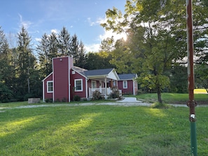 A red house with a front porch, surrounded by a grassy yard and trees. - Long Term Fully Furnished Country Farmhouse Ranch w/ pond in Rock Creek, Ohio (Rock Creek)