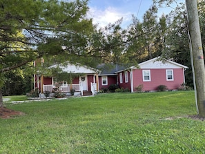 A two-story house with a front porch, a small front yard, and a red exterior. - Long Term Fully Furnished Country Farmhouse Ranch w/ pond in Rock Creek, Ohio (Rock Creek)