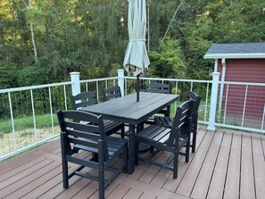 A wooden deck with a table and chairs, surrounded by a white railing, overlooking a forested area. - Long Term Fully Furnished Country Farmhouse Ranch w/ pond in Rock Creek, Ohio (Rock Creek)