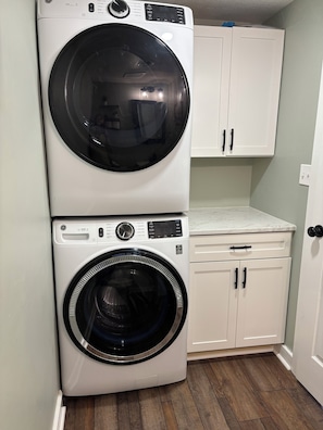 A stacked washer and dryer unit in a laundry room with white cabinets and a marble countertop. - Long Term Fully Furnished Country Farmhouse Ranch w/ pond in Rock Creek, Ohio (Rock Creek)