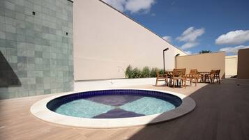 Piscina com borda revestida em azulejo, rodeada por um deck de madeira e móveis de exterior.