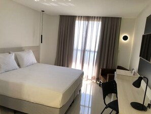 Habitación de hotel con una cama grande, un escritorio con silla, una lámpara de escritorio y una ventana con cortinas.