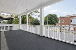 A covered outdoor area with a dark floor, white railing, and a view of a street with buildings and trees. - 2BR Lower Unit Near Niagara Falls | Free WiFi (Niagara Falls)
