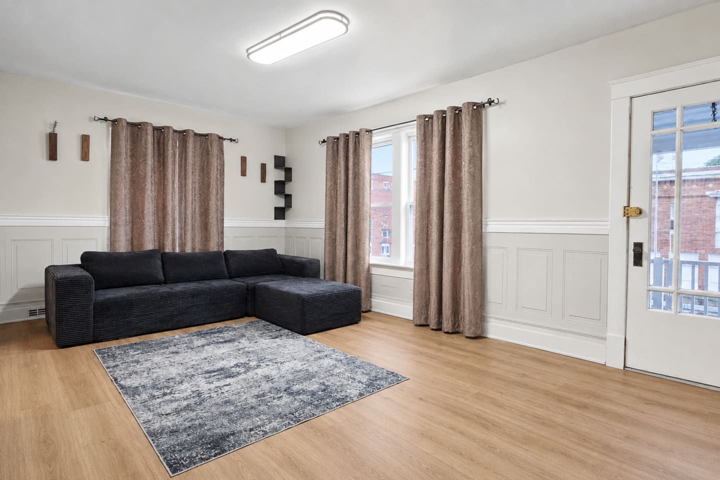 A modern living room with a sectional sofa, a patterned rug, and a door with a view of buildings.
