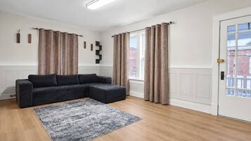 A modern living room with a sectional sofa, a patterned rug, and a door with a view of buildings.