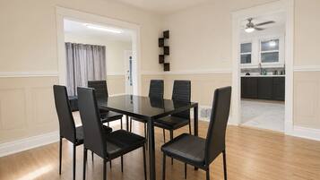 A dining area with a rectangular table and six chairs, a kitchen in the background, and a ceiling fan.