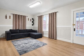 Una sala moderna con un sofá modular, un tapete estampado y una puerta con vista a edificios.
