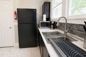Een keuken met een zwarte koelkast, een magnetron, een koffiezetapparaat en een roestvrijstalen spoelbak met een afwasschaal.