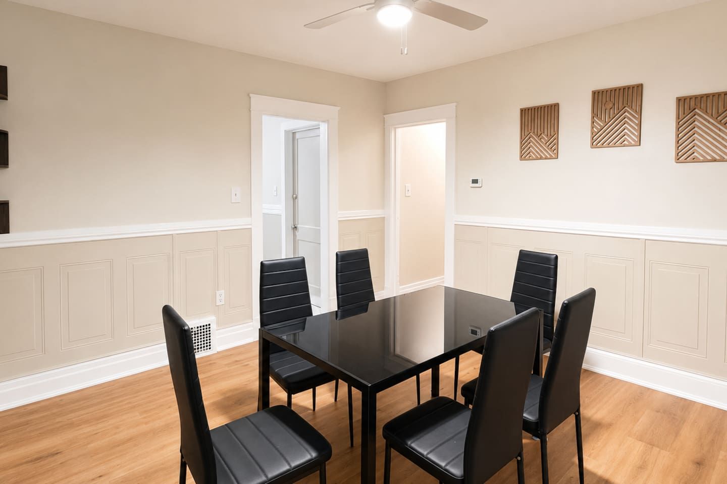 A conference room with a glass table, black chairs, wooden flooring, and decorative wall panels.