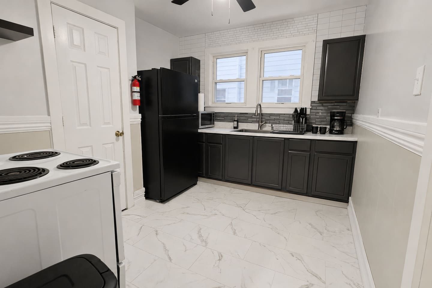 A kitchen with a white stove, black refrigerator, and dark cabinets.