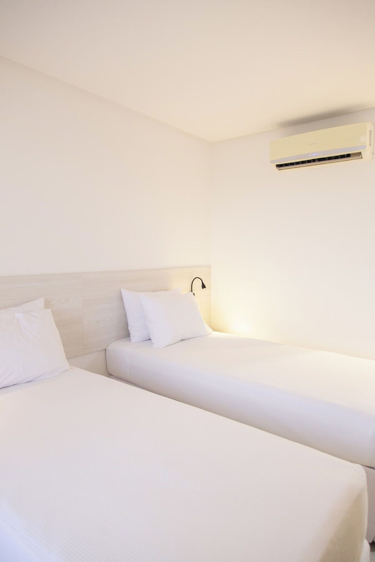 Ein Hotelzimmer mit zwei Einzelbetten, einer Kopfteil und einer wandmontierten Klimaanlage.