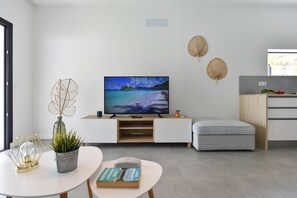 Ein modernes Wohnzimmer mit einem Flachbildfernseher, einer weißen Vitrine, einem grauen Sofa, einem runden Couchtisch und einem kleinen Esstisch.
