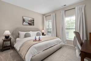 Een hotelkamer met een bed, twee nachtkastjes, een lamp, een schilderij aan de muur en een raam met gordijnen.