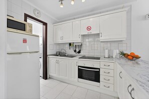 A modern kitchen with white cabinetry, a built-in oven, a sink, and a fruit bowl on the counter. - Bungalow Island Village (Costa Adeje)