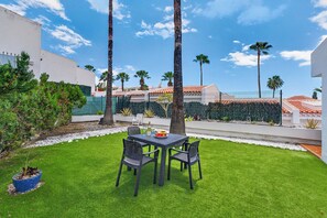 A patio with a table and chairs, surrounded by a well-maintained lawn and palm trees. - Bungalow Island Village (Costa Adeje)