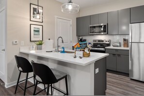 A modern kitchen with a central island, bar stools, a microwave, an oven, and a refrigerator. - New Albany 2BR Near Intel Easton Pets OK (Westerville)