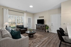 A living room with a sofa, armchair, coffee table, and a flat-screen TV on a cabinet. - New Albany 2BR Near Intel Easton Pets OK (Westerville)