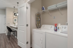 A laundry room with a washing machine, dryer, ironing board, and ironing supplies. - New Albany 2BR Near Intel Easton Pets OK (Westerville)