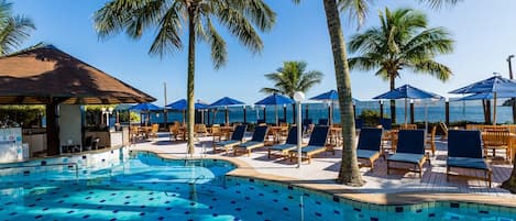 A pool area with lounge chairs and umbrellas, surrounded by palm trees.