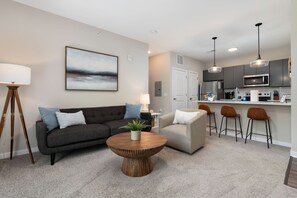 A modern living room with a dark grey sofa, a round coffee table, and a painting on the wall. - The Nook New Albany Area Balcony (Westerville)