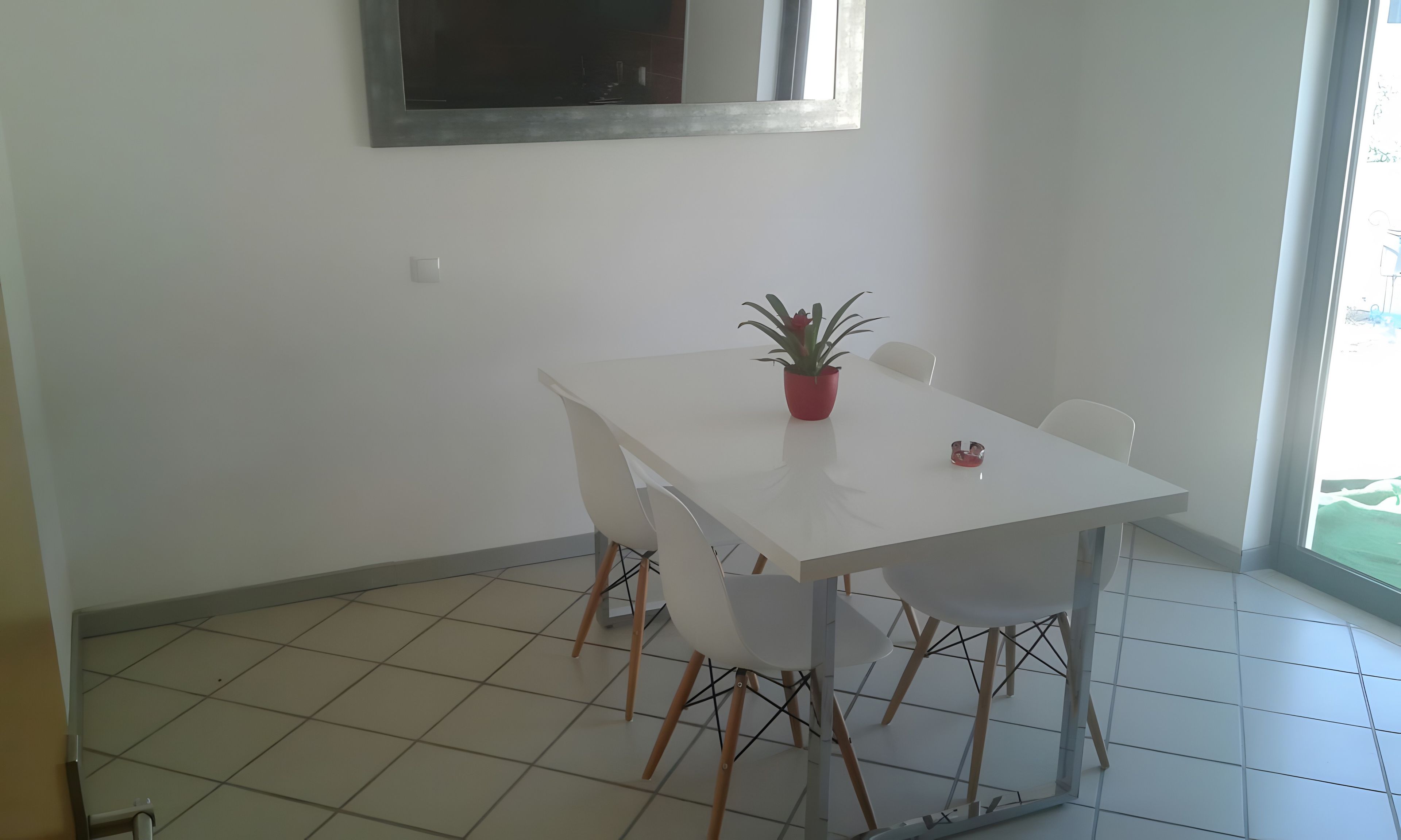 Un comedor con una mesa blanca, cuatro sillas, una planta en maceta y un ventanal con vistas.