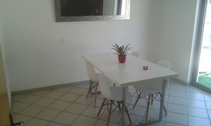 A dining area with a white table, four chairs, a potted plant, and a window with a view.