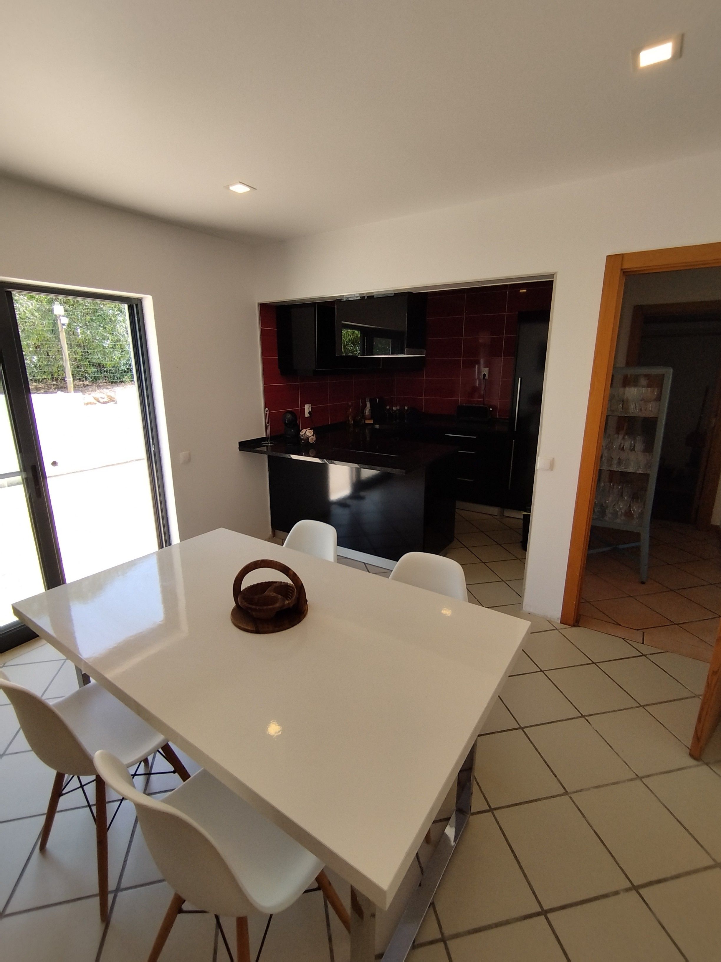 Una cucina moderna con piastrelle rosso scuro, un tavolo da pranzo bianco con sedie e un'isola cucina a vista.