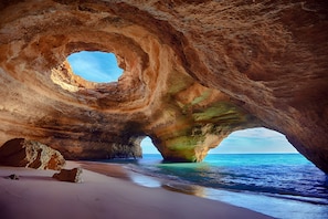 A natural rock formation with a circular opening, a sandy beach, and the sea.