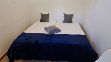 Een nette, kleine kamer met een bed, twee kussens, een nachtkastje en een stoel.