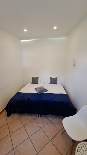 Una habitación pequeña y limpia con una cama, dos almohadas, una mesita de noche y una silla.