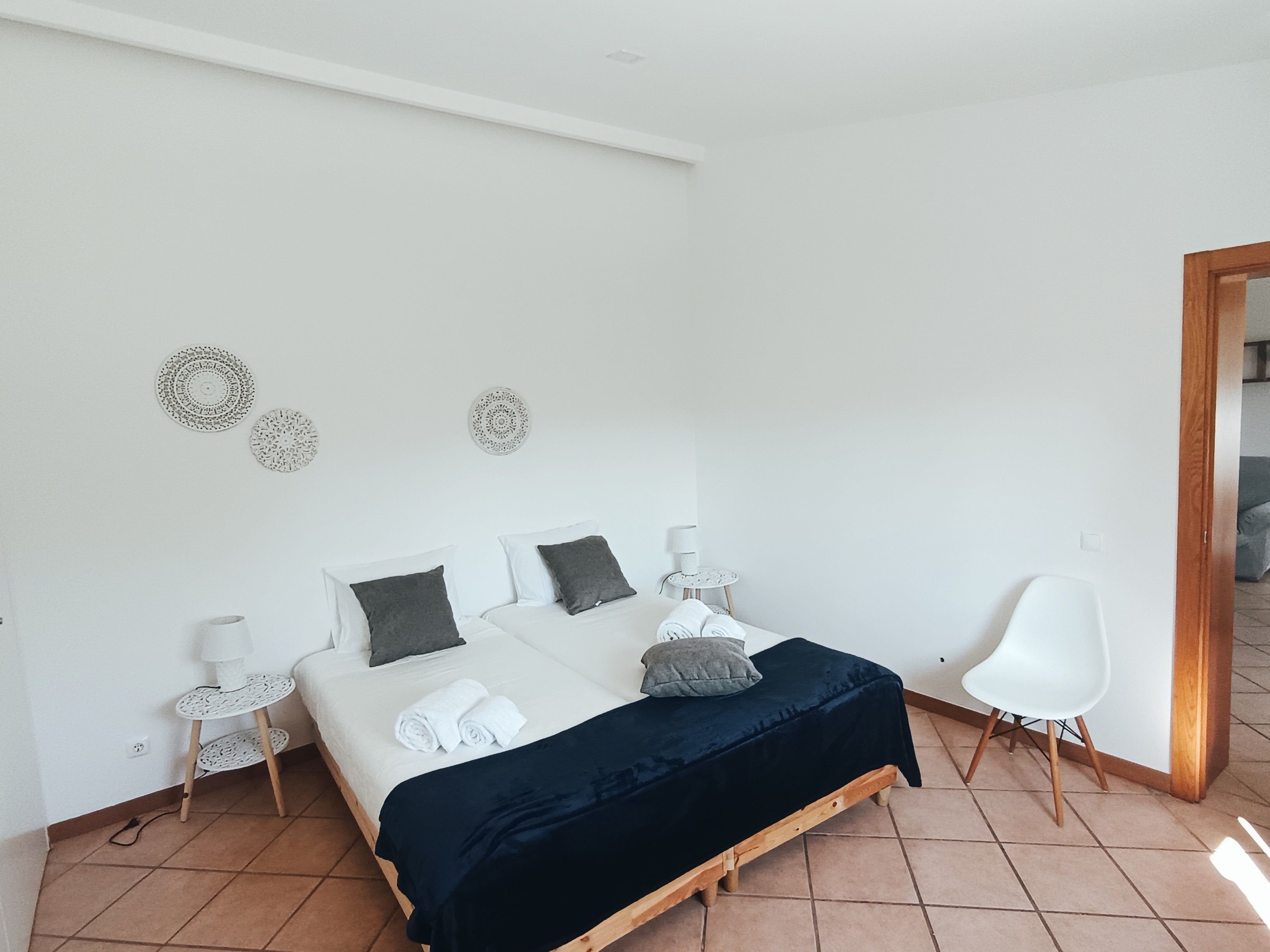 Un dormitorio con cama, mesitas de noche, decoración en la pared, una silla y suelo de madera.