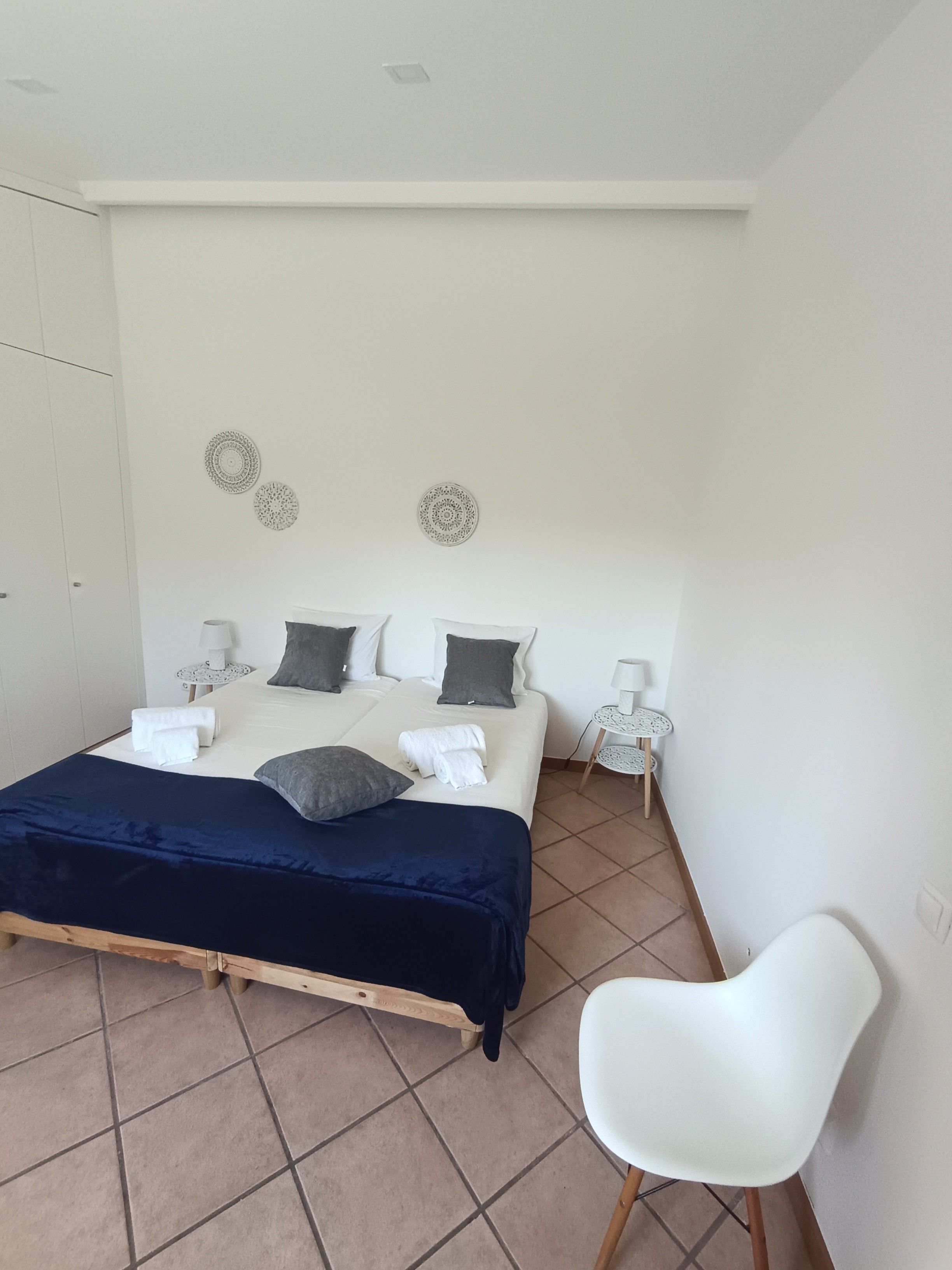 Un dormitorio con cama, mesitas de noche, una silla y decoración en la pared.
