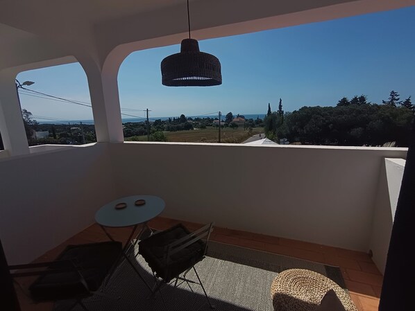 Un balcon avec une table et des chaises, un luminaire suspendu et une vue sur un paysage arboré avec des bâtiments.