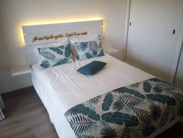 A bed with a headboard, white bedding, and a tropical leaf pattern.