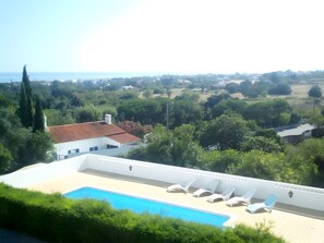 Ein Poolbereich mit Liegestühlen, freier Aussicht auf die umliegende Landschaft und ein Gebäude mit rotem Ziegeldach.