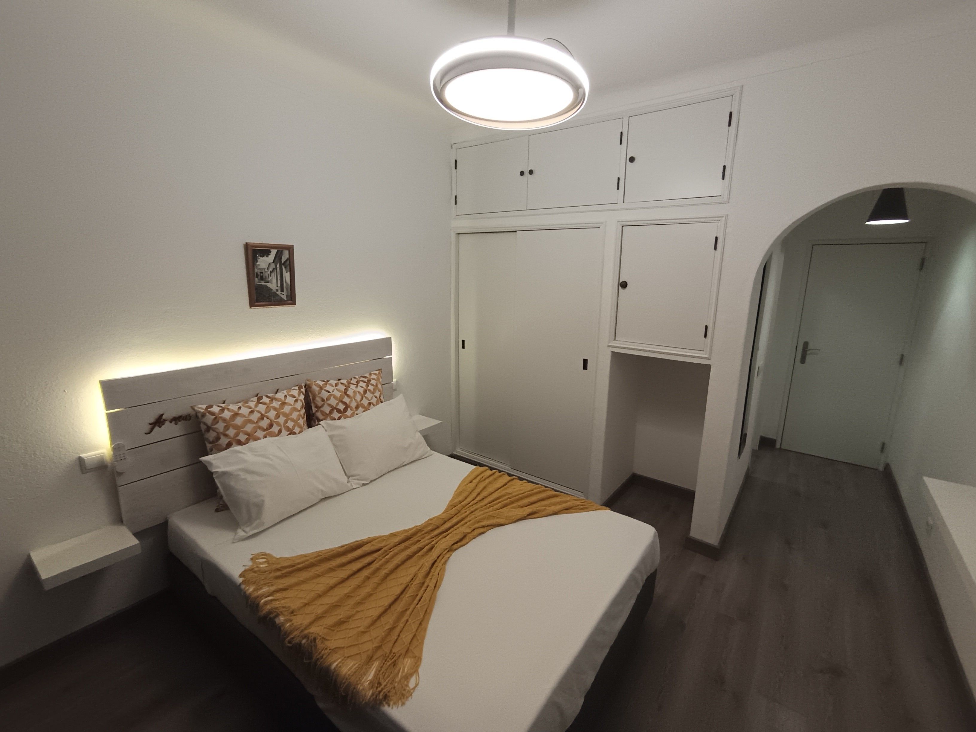 Ein Schlafzimmer mit Bett, Nachttisch, Kleiderschrank und einem anliegenden Flur.